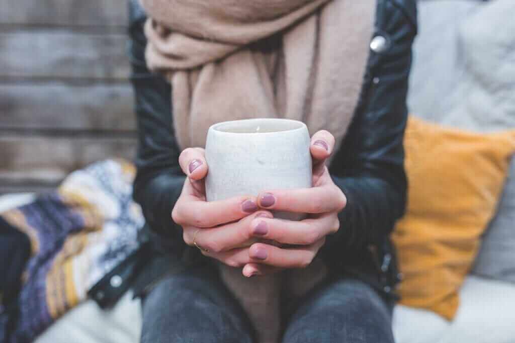 Une tasse de thé chaude pour se soulager et se remettre sur pied Plan sur une personne portant une écharpe et tenant une tasse de thé chaude.